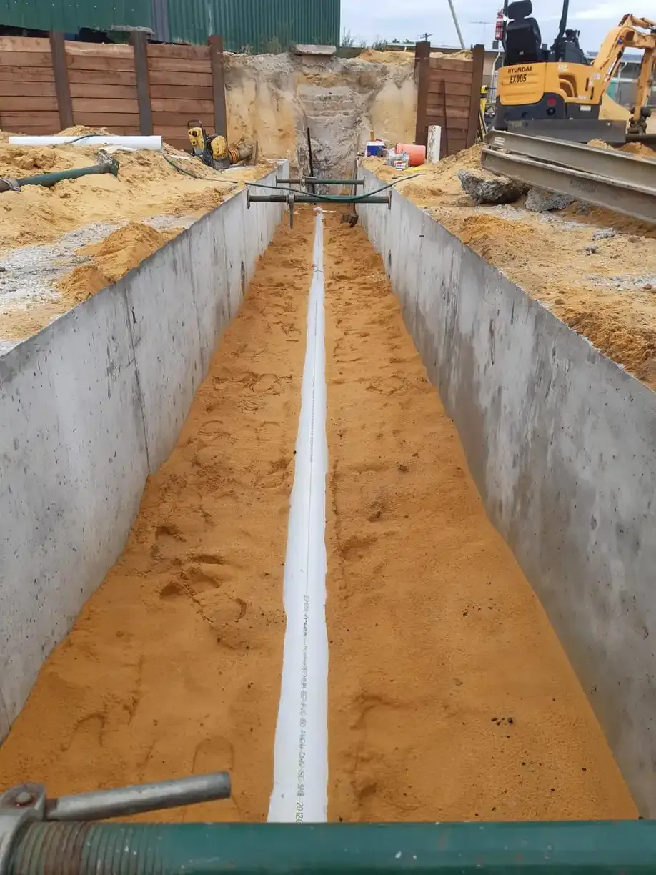 A new PVC drain line bedded in sand between concrete trench walls.